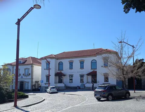 Edifício branco da Biblioteca Municipal com telhado de telha vermelha e praça calcetada em frente