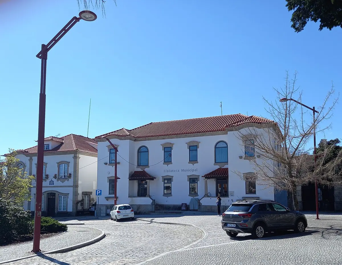 Edifício branco da Biblioteca Municipal com telhado de telha vermelha e praça calcetada em frente