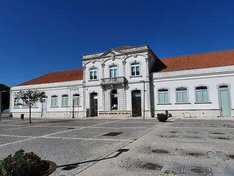 Fachada branca da Biblioteca Municipal de Palmela, com telhado de telha e largo calcetado em frente.