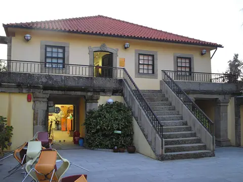 Edifício do Museu do Brinquedo com escadaria de pedra, varanda e entrada iluminada ao nível inferior