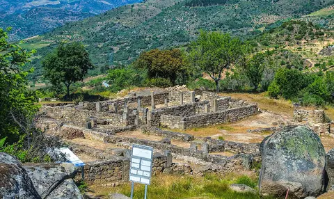 Ruínas de estruturas em pedra da estação arqueológica do Prazo, rodeadas de vegetação e colinas