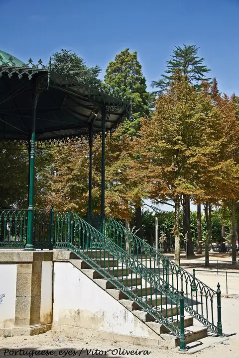 Coreto de ferro verde com escadaria no Jardim Público de Chaves, rodeado de árvores.