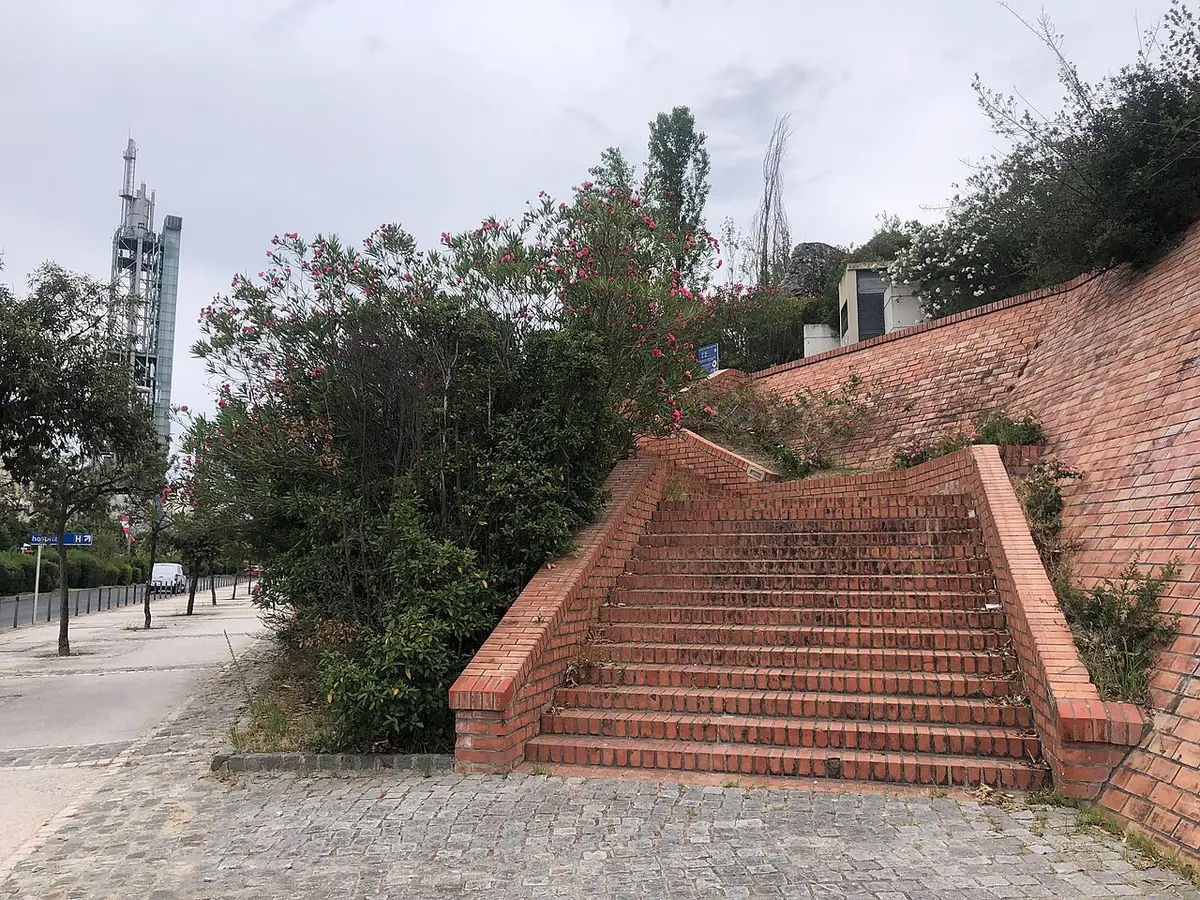Escadaria de tijolo com muro e arbustos floridos no acesso ao Jardim do Cabeço das Rolas