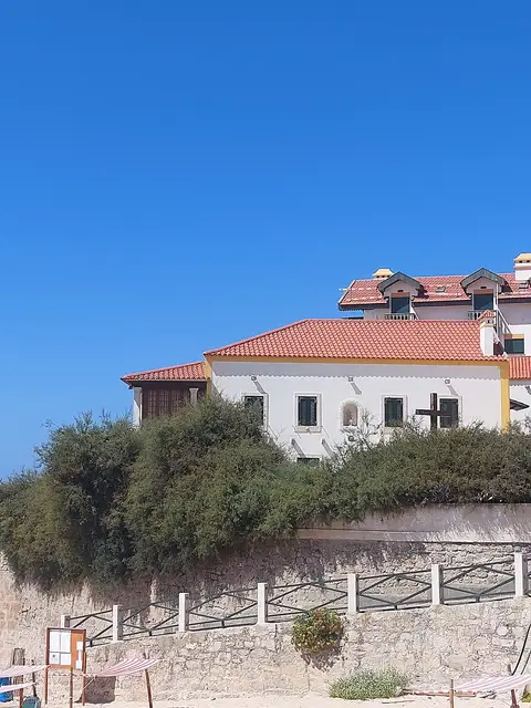 Fachada branca com telhado vermelho da Casa Museu Afonso Lopes Vieira, sobre muro de pedra e vegetação.
