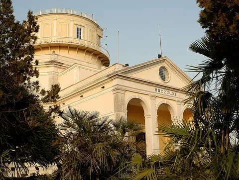 Edifício do Observatório Astronómico de Lisboa, com cúpula e pórtico de arcos, rodeado de palmeiras