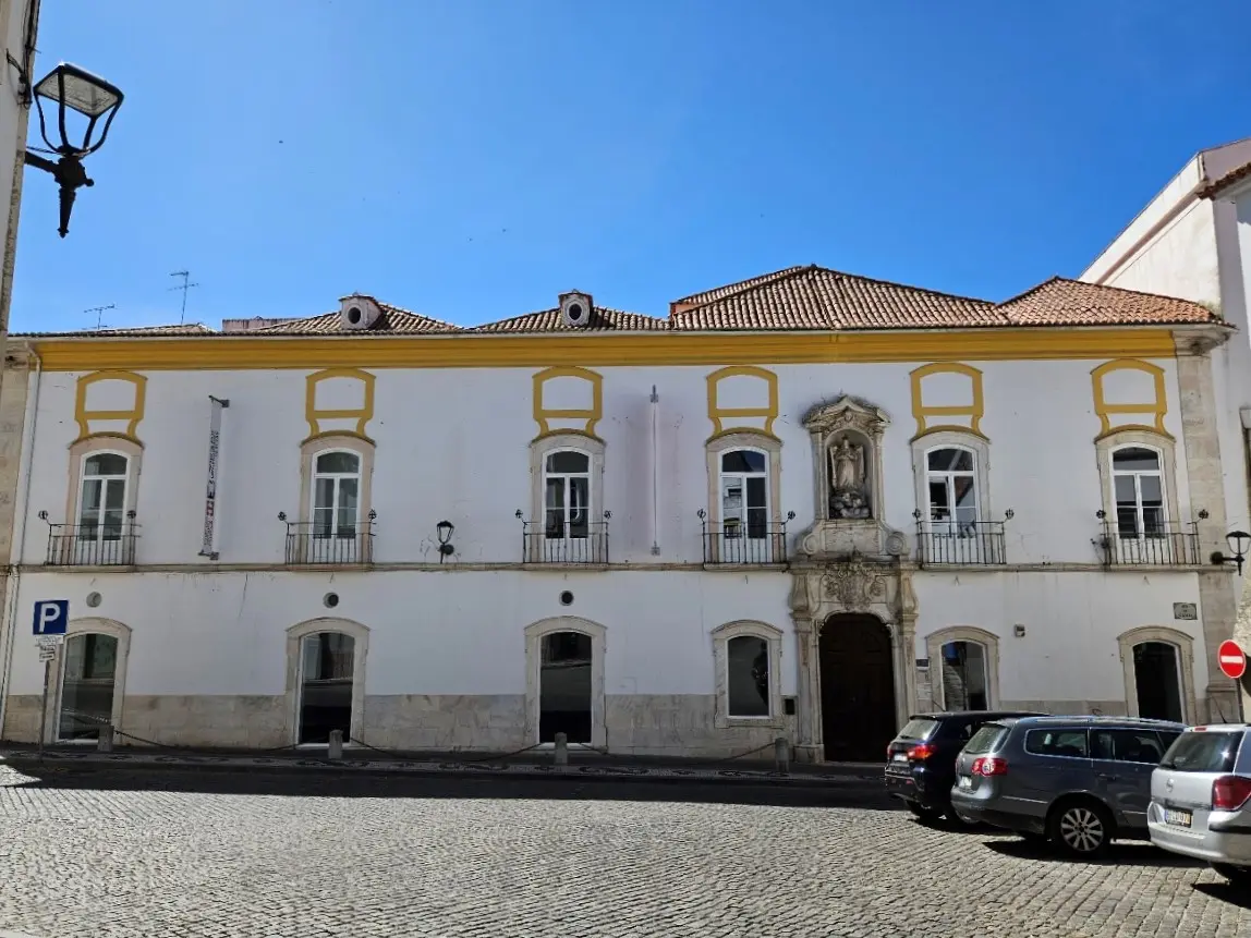 Fachada branca e amarela do Museu de Arte Contemporânea de Elvas, com portal barroco e carros estacionados.