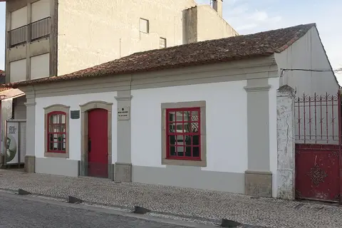 Fachada branca da casa museu Júlio Dinis, em Ovar, com porta e janelas de caixilharia vermelha