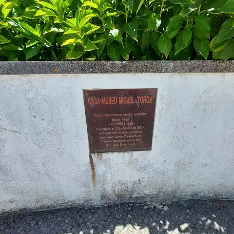 Placa identificativa da Casa-Museu Miguel Torga num muro, com sebe verde por cima