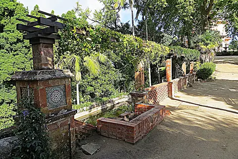 Recanto ajardinado com fonte e azulejos decorativos, pérgula com trepadeiras e vegetação exuberante no Parque de Monserrate