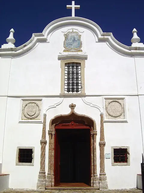 Fachada branca da Capela de Nossa Senhora das Salvas, em Sines, com portal manuelino e painel de azulejos