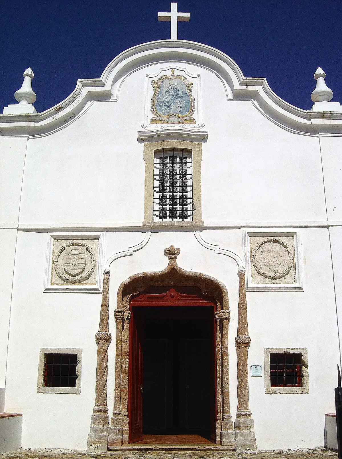 Fachada branca da Capela de Nossa Senhora das Salvas, em Sines, com portal manuelino e painel de azulejos