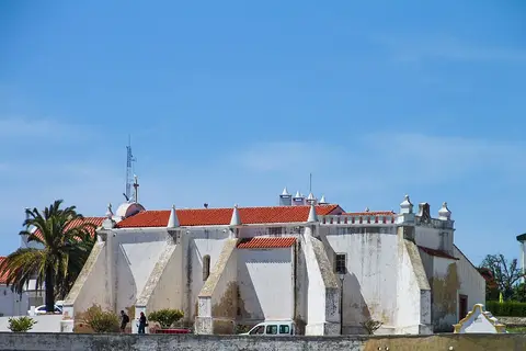 Exterior caiado da Ermida de Nossa Senhora das Salvas, em Sines, com telhado vermelho e pináculos.