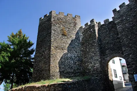 Muralhas e torre de pedra com ameias do Castelo de Bragança, com arco de entrada, sob céu azul.