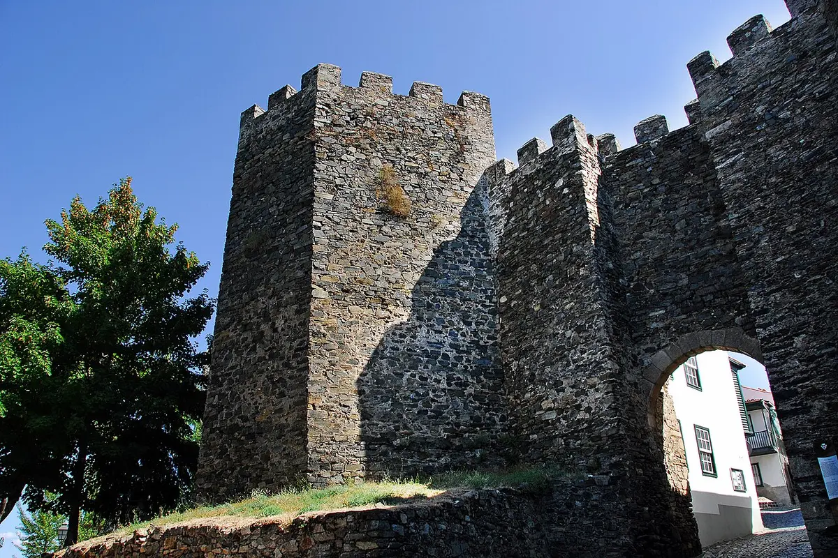 Muralhas e torre de pedra com ameias do Castelo de Bragança, com arco de entrada, sob céu azul.