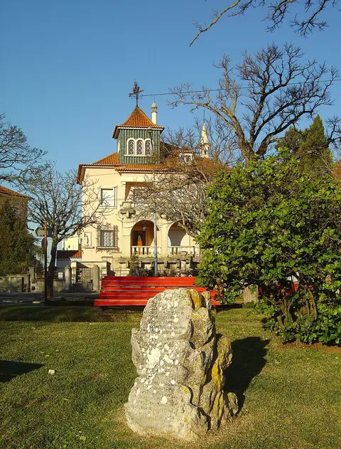 Jardim do Penedo da Saudade em Coimbra, com pedra gravada, relva e edifício histórico ao fundo