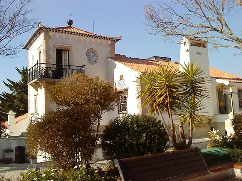 Casa Roque Gameiro na Amadora, edifício branco com painel de azulejos, varanda em ferro e jardim.