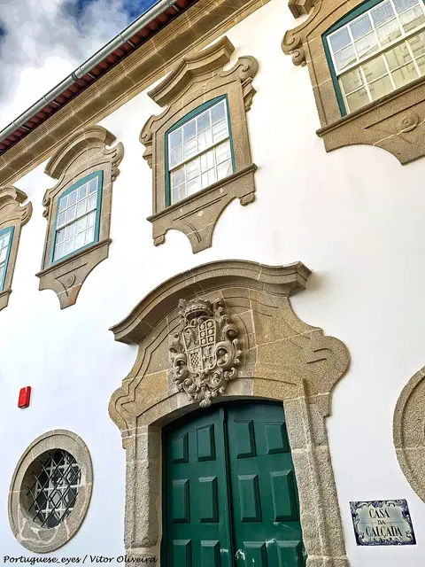 Fachada branca da Casa da Calçada, em Viseu, com portal barroco em granito, brasão e porta verde.