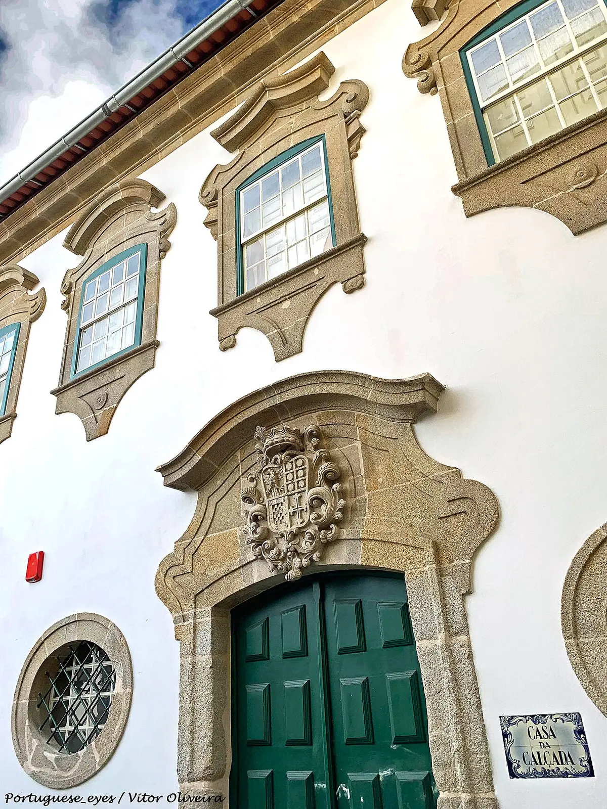 Fachada branca da Casa da Calçada, em Viseu, com portal barroco em granito, brasão e porta verde.