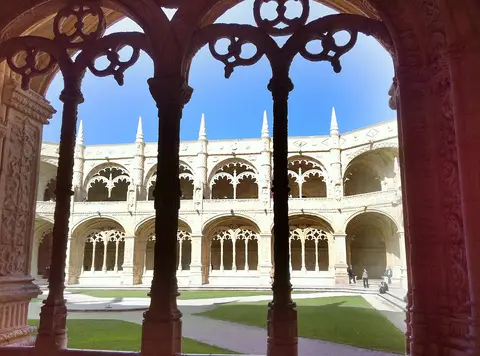 Claustro manuelino do Mosteiro dos Jerónimos visto através de arcos rendilhados, com relvado ao centro