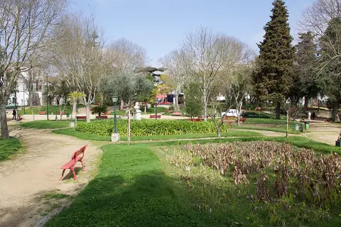 Jardim Público de Évora com relvados, canteiros, bancos vermelhos e árvores num dia de sol.