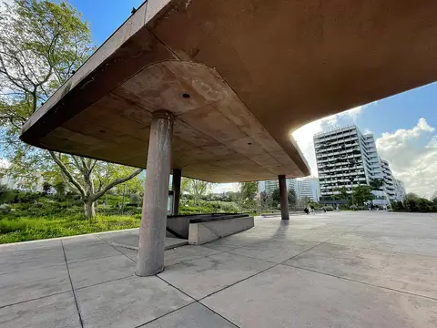 Estrutura de betão com pilares no Parque Gonçalo Ribeiro Telles, com jardim e prédios ao fundo