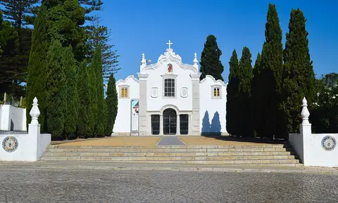 Fachada branca da igreja do Convento dos Capuchos, ladeada por ciprestes, com escadaria em pedra.