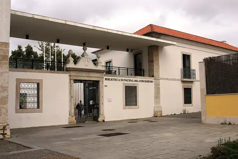 Entrada da Biblioteca Municipal Orlando Ribeiro, em Telheiras, com portão de ferro e letreiro na fachada branca