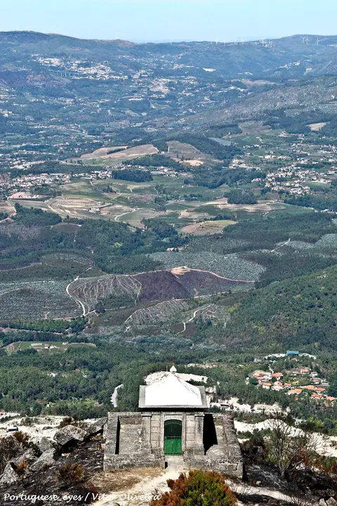 Pequena capela de pedra no alto da serra, com vista sobre o vale e aldeias ao fundo