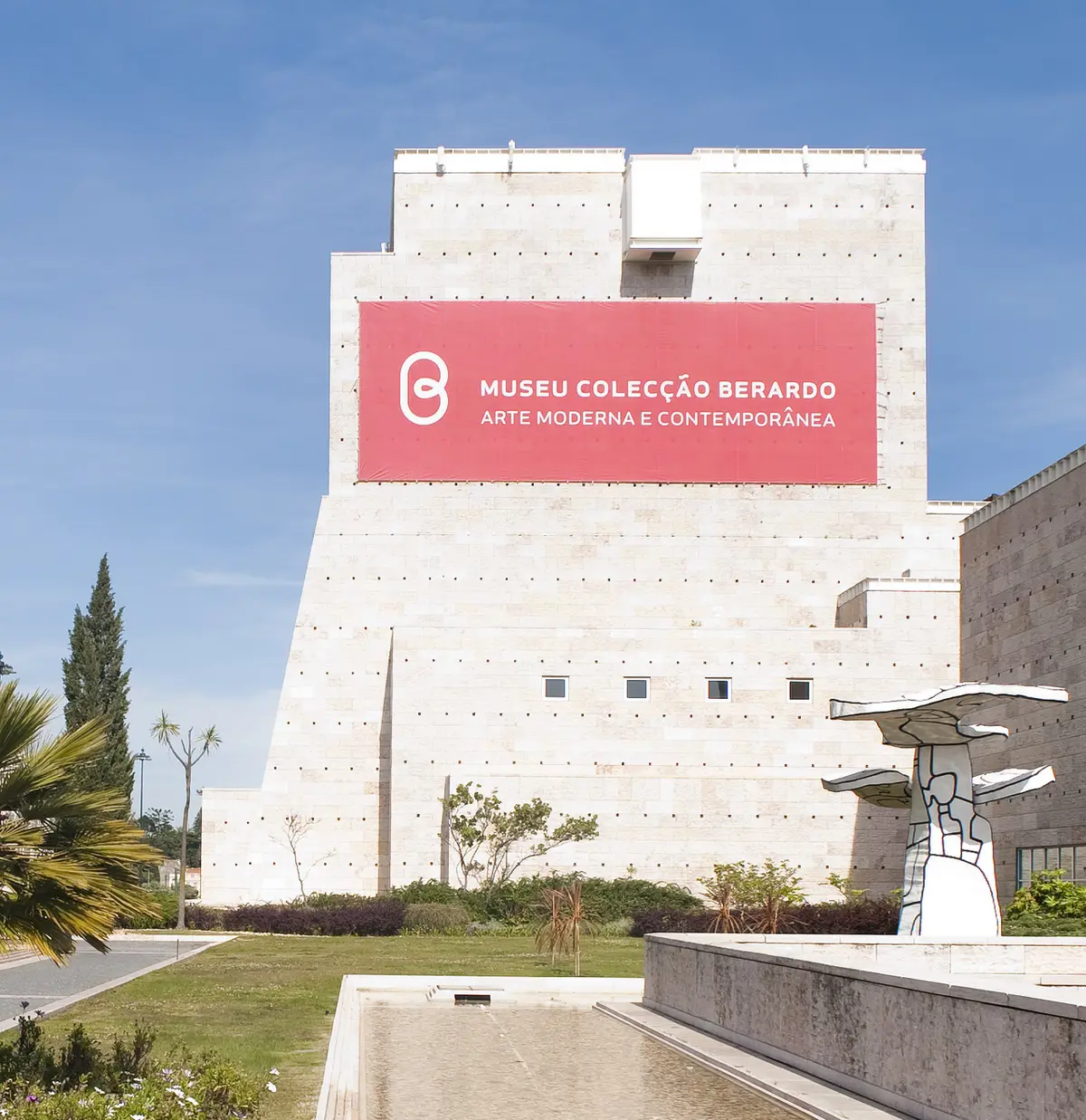 Fachada em pedra do Museu Colecção Berardo, no CCB, com faixa vermelha e escultura no jardim