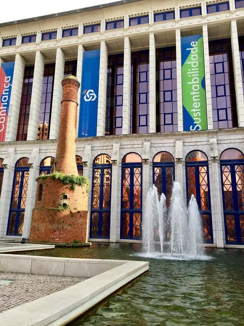 Fachada da Caixa Geral de Depósitos com chaminé de tijolo e repuxos de água no lago exterior