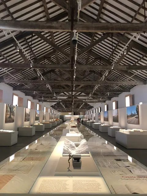 Sala de exposições da Casa da Arquitetura com teto de madeira, vitrinas e maquetas.