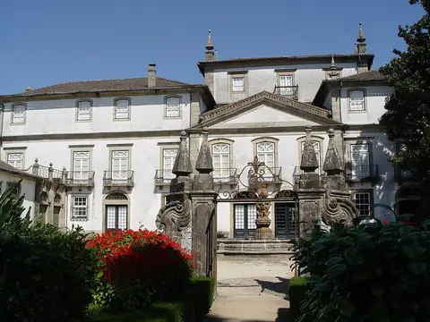 Fachada do Palácio dos Biscainhos vista do jardim, com portão em ferro e canteiros de flores vermelhas