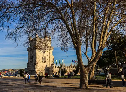 Jardim junto à Torre de Belém, com árvores grandes e pessoas a passear ao fim da tarde