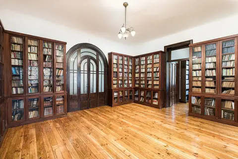 Sala de biblioteca com estantes de madeira envidraçadas, soalho em madeira e candeeiro de teto