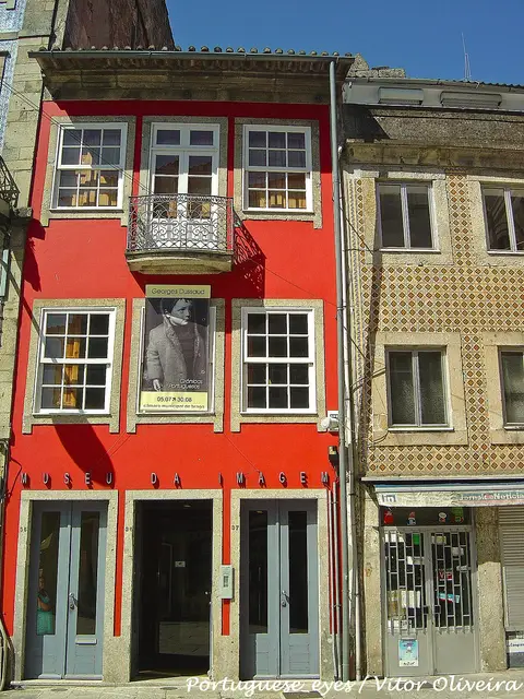 Fachada vermelha do Museu da Imagem, em Braga, com varanda de ferro e cartaz de exposição