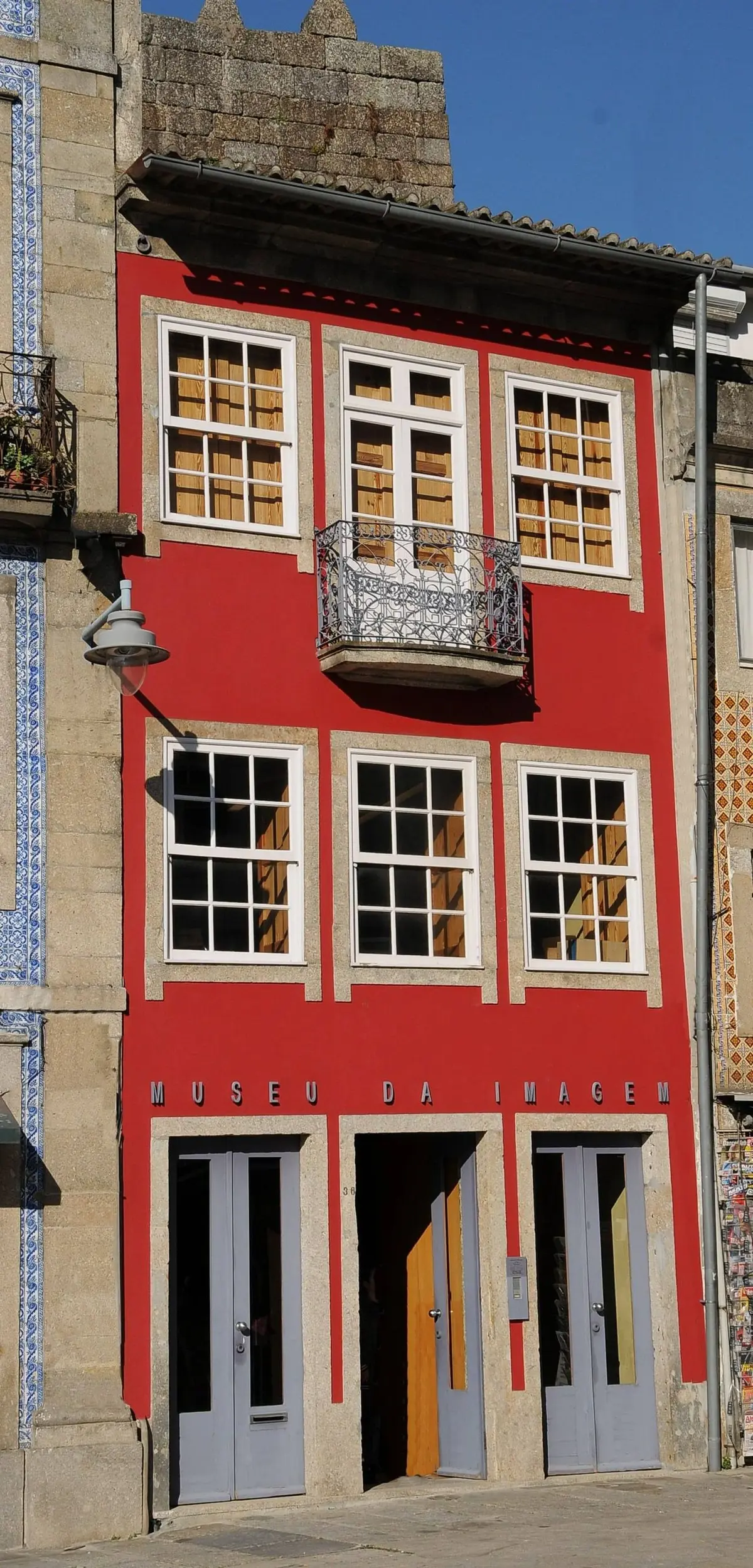 Fachada vermelha do Museu da Imagem, em Braga, com varanda de ferro e portas no piso térreo