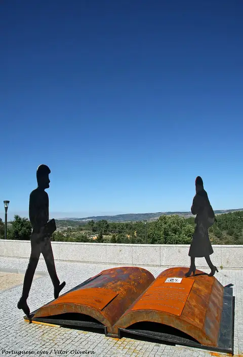 Escultura em metal de livro aberto com silhuetas humanas junto à Biblioteca Municipal de Celorico da Beira