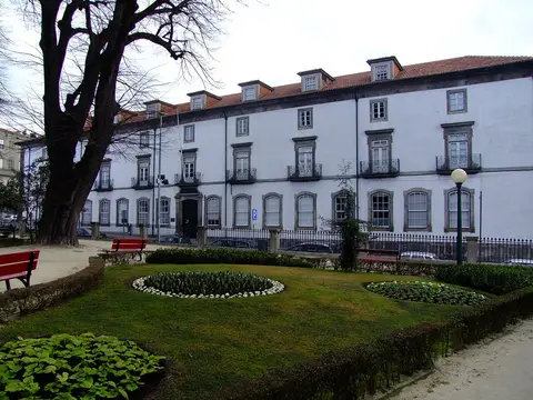 Edifício branco da Biblioteca Pública Municipal do Porto visto do jardim com canteiros e bancos