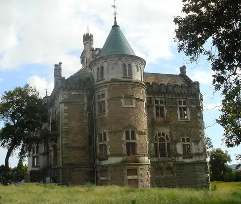 Fachada norte do Castelo da Dona Chica, com torre cónica e paredes de pedra, rodeado de relva e árvores.