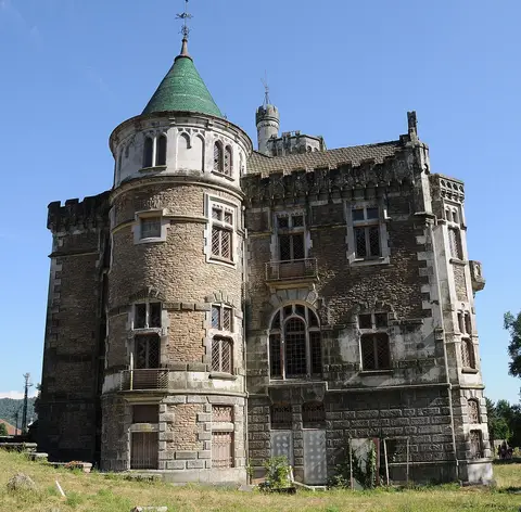 Fachada do Castelo da Dona Chica em pedra, com torre circular e cúpula verde, sob céu azul