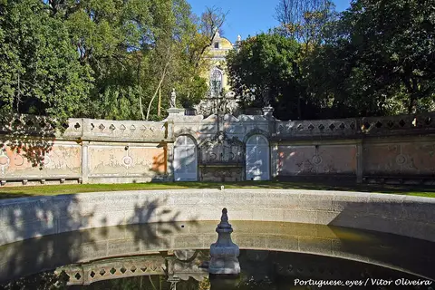 Lago e muro ornamental com estátuas na Tapada das Necessidades, rodeados de árvores, em Lisboa