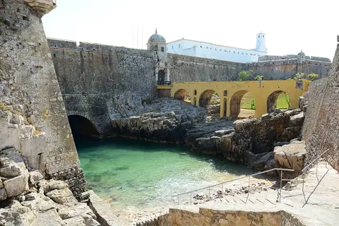 Entrada da Fortaleza de Peniche com ponte de arcos amarela sobre água verde e muralhas de pedra