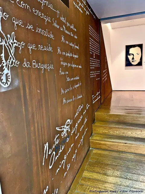 Interior de museu com parede em metal oxidado gravada com letras de fado e retrato ao fundo