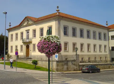 Edifício histórico da biblioteca em Viseu, com fachada clara, telhado de telha e canteiro de flores em primeiro plano